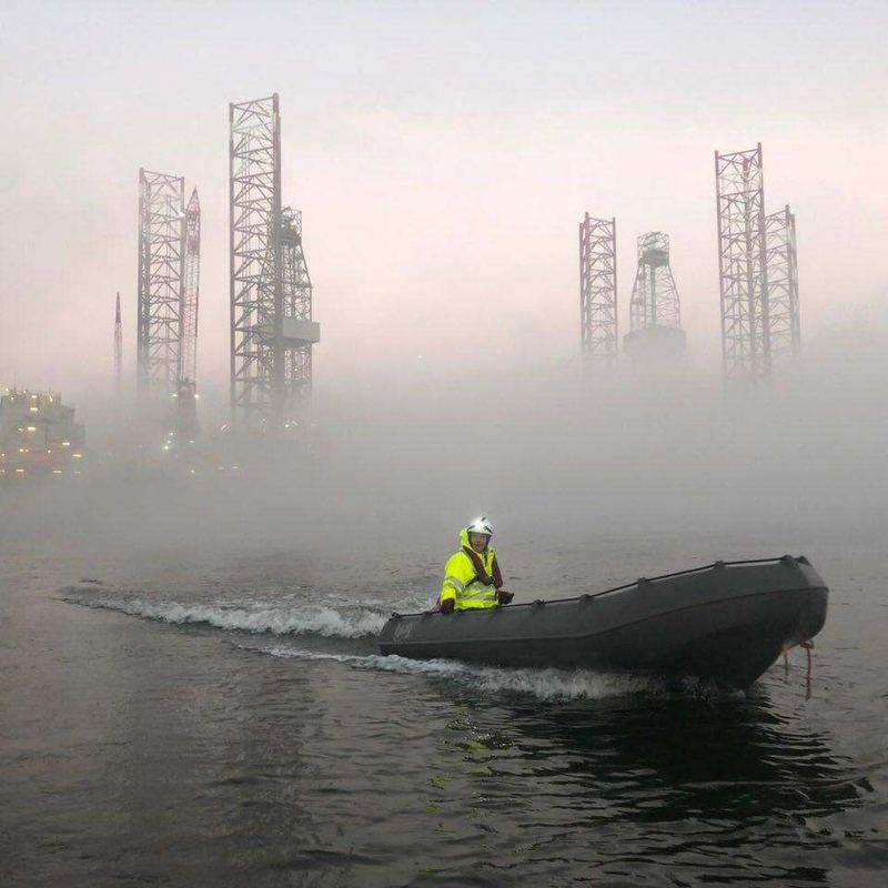 Safety boat and crew on misty water beside industrial structures